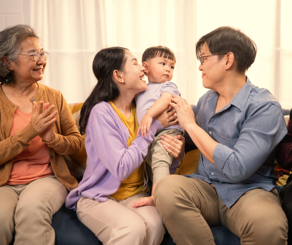 Meerdere familieleden lachen samen rond een baby in gezinstherapie bij Maduh Praktijk